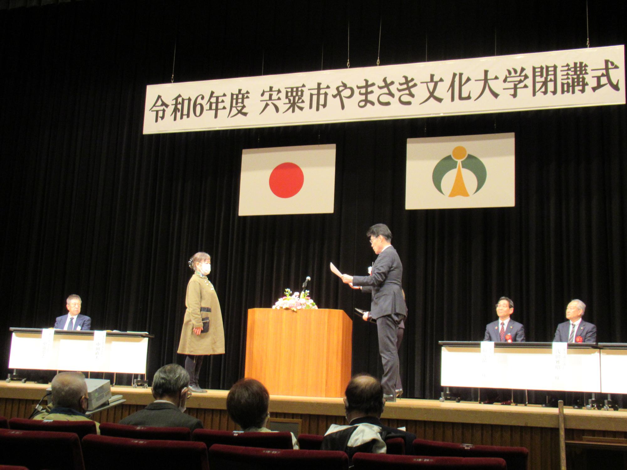 修了証書授与で代表者の学生が学園長より賞状を授与されている写真