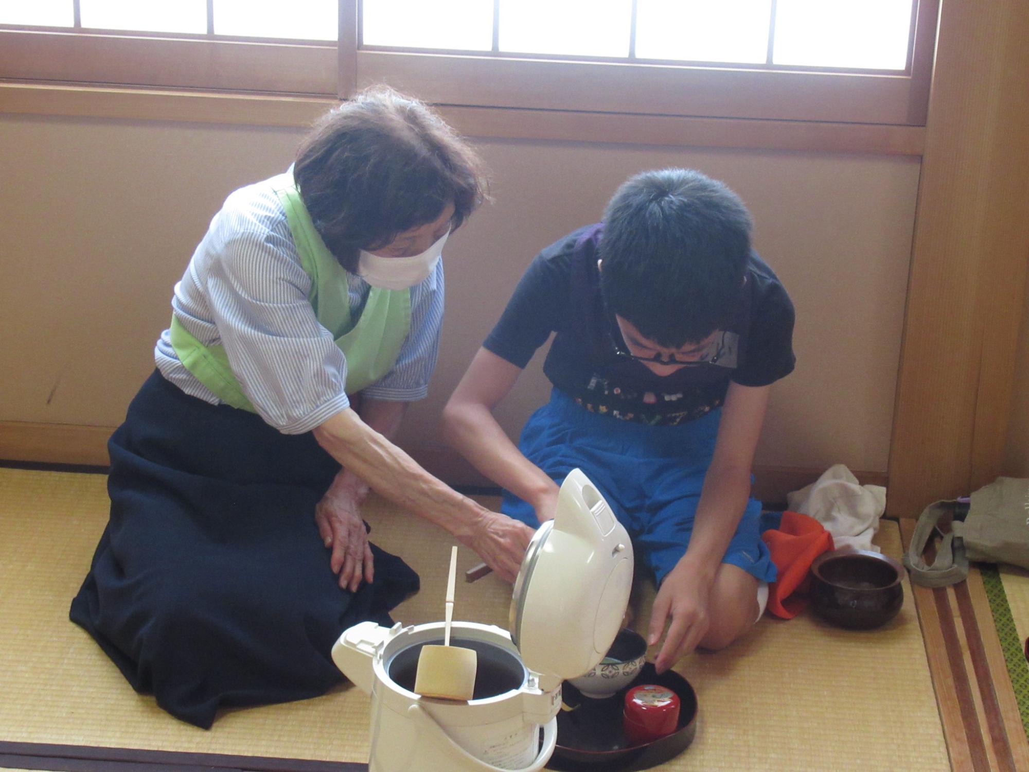 講師の方に教わりながら柄杓でお湯をくみ上げる参加者