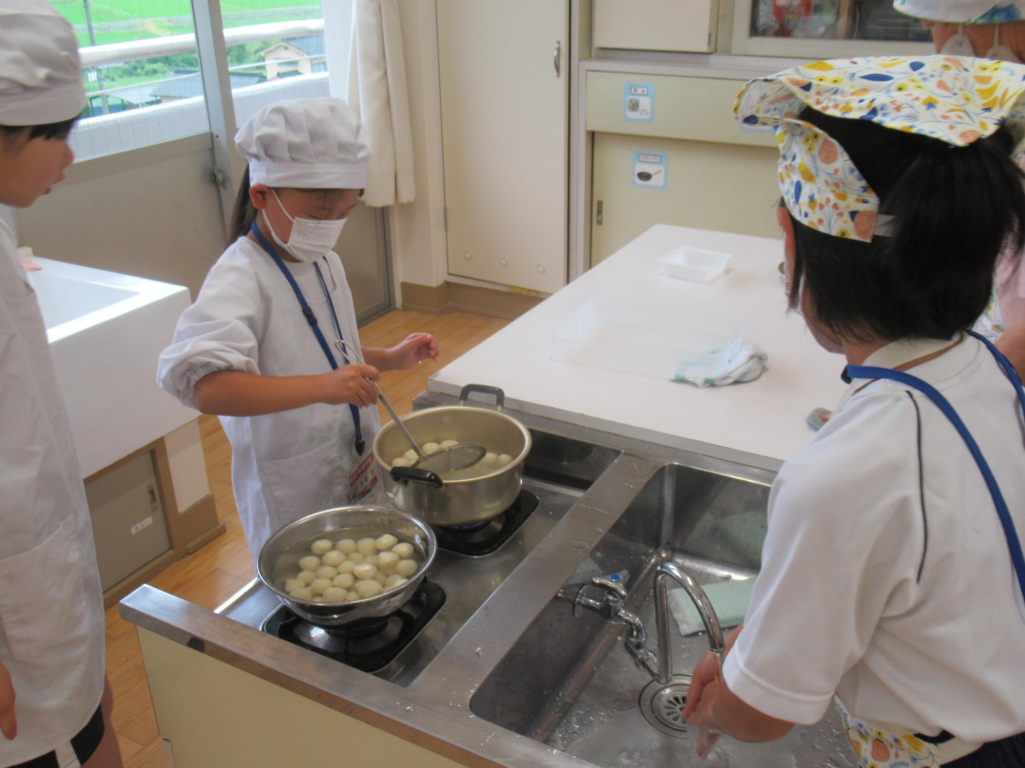 茹で上がった白玉を鍋からすくい取っている子どもたちの写真