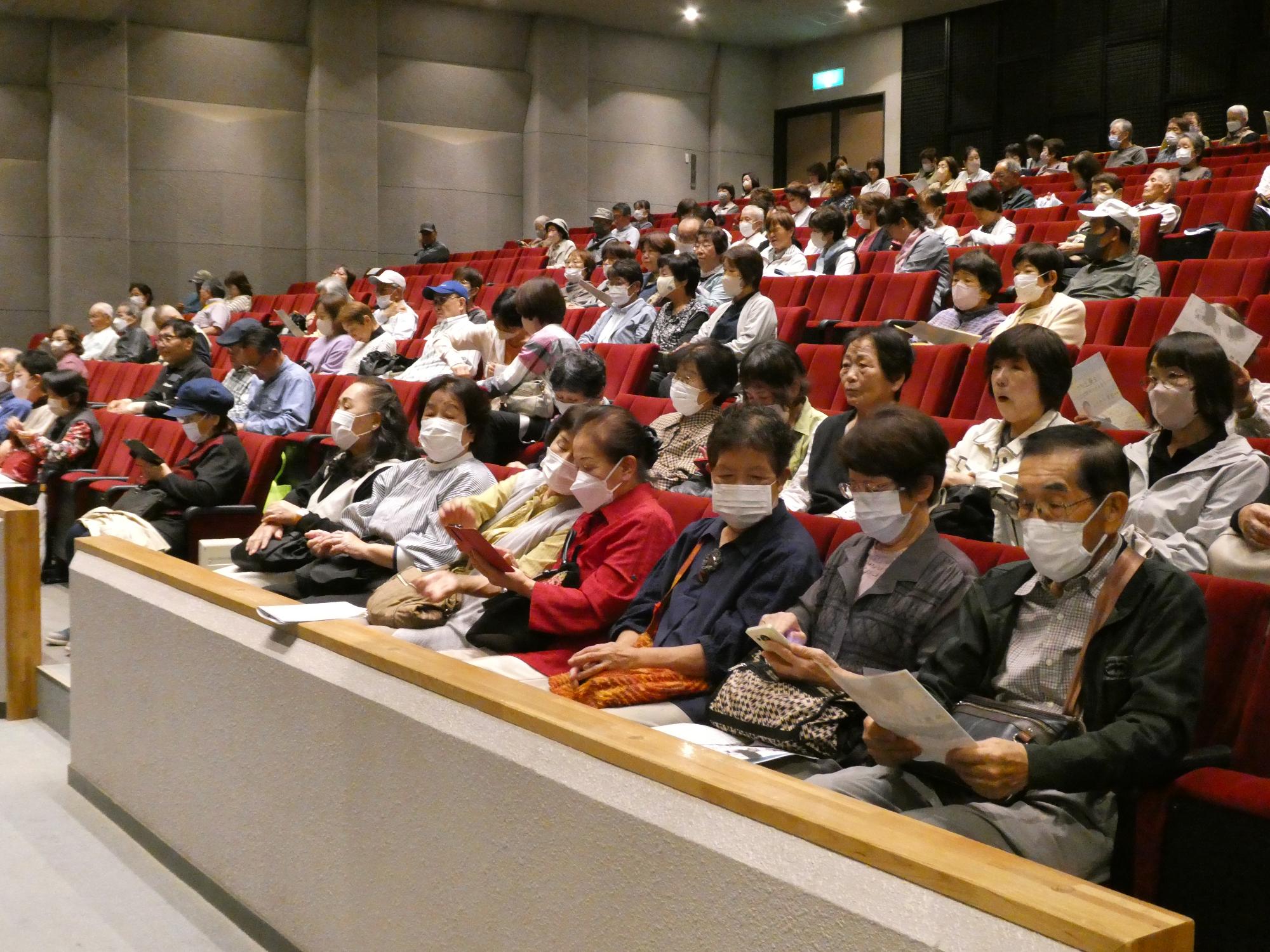 山崎文化会館ホールの客席に座って映画鑑賞講座開始前に談笑する参加者の写真