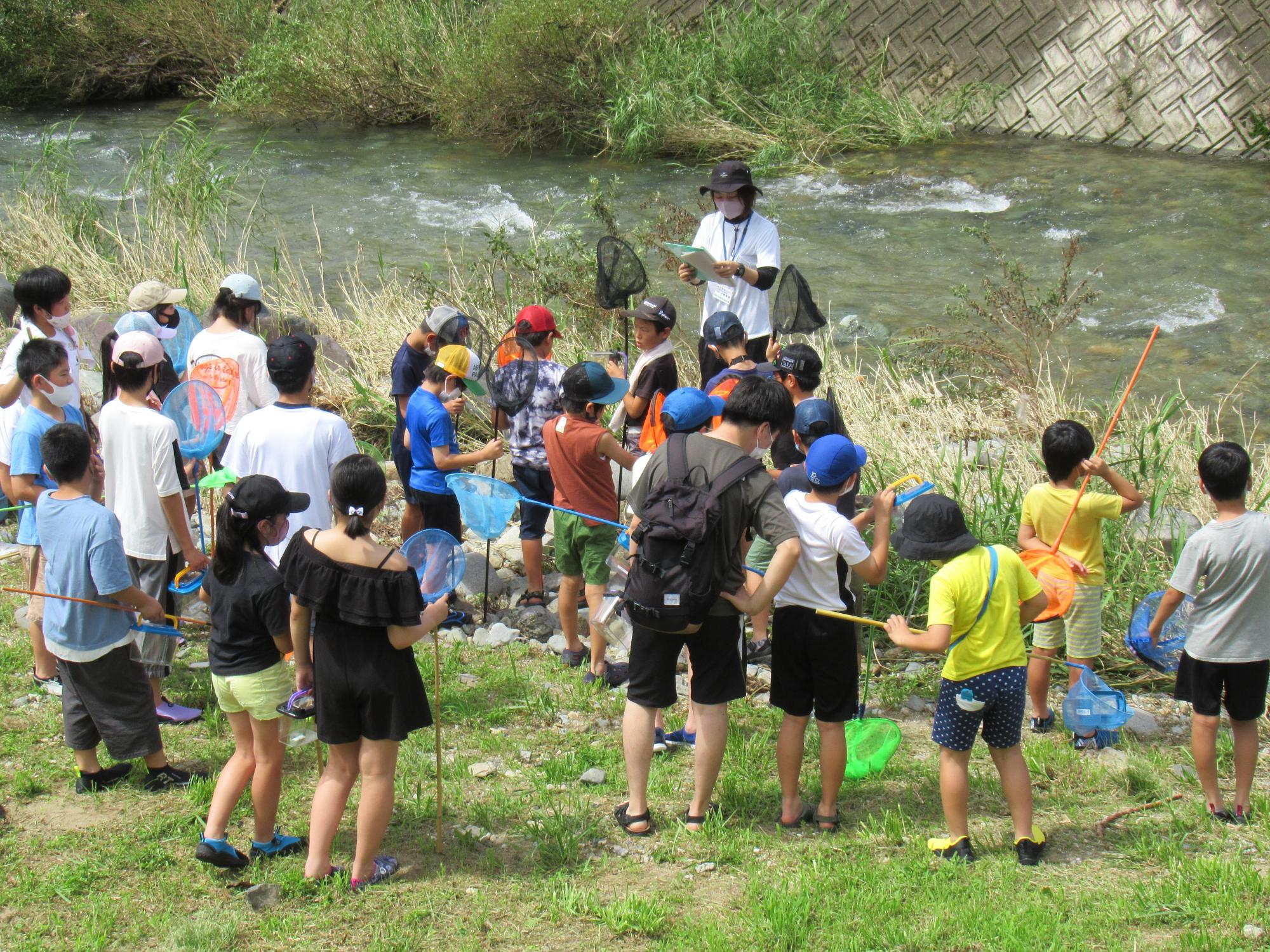 伊沢川探検で伊沢川に入る前にサポーターから注意事項を聞く子どもたちの写真