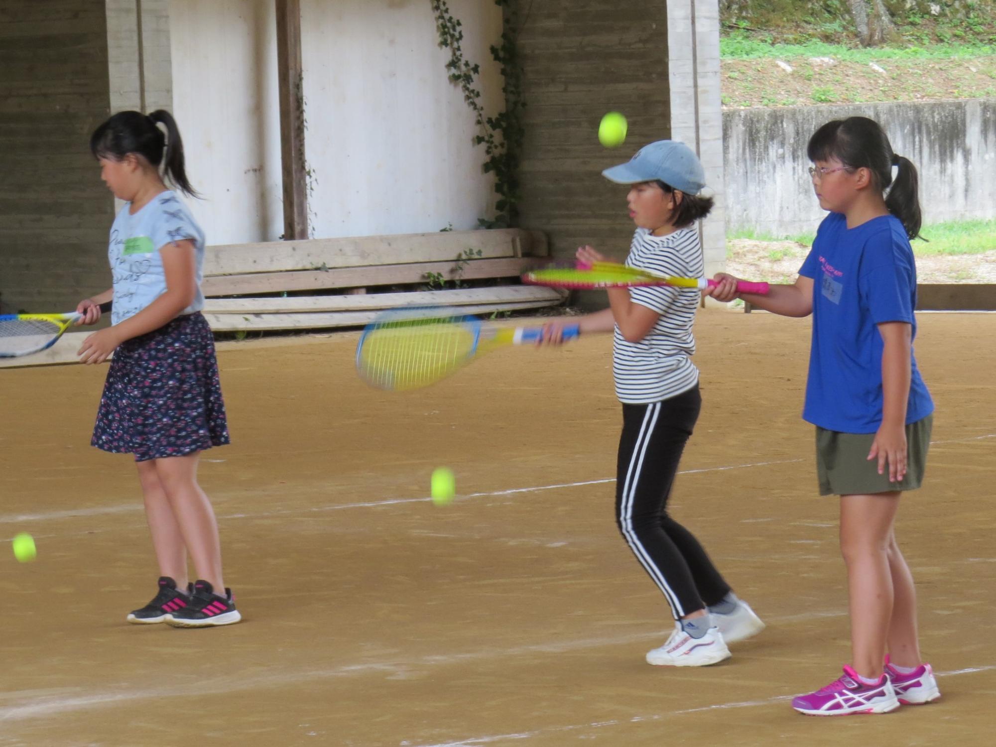 テニスラケットとボールで打ち方の練習をする子どもたちの写真
