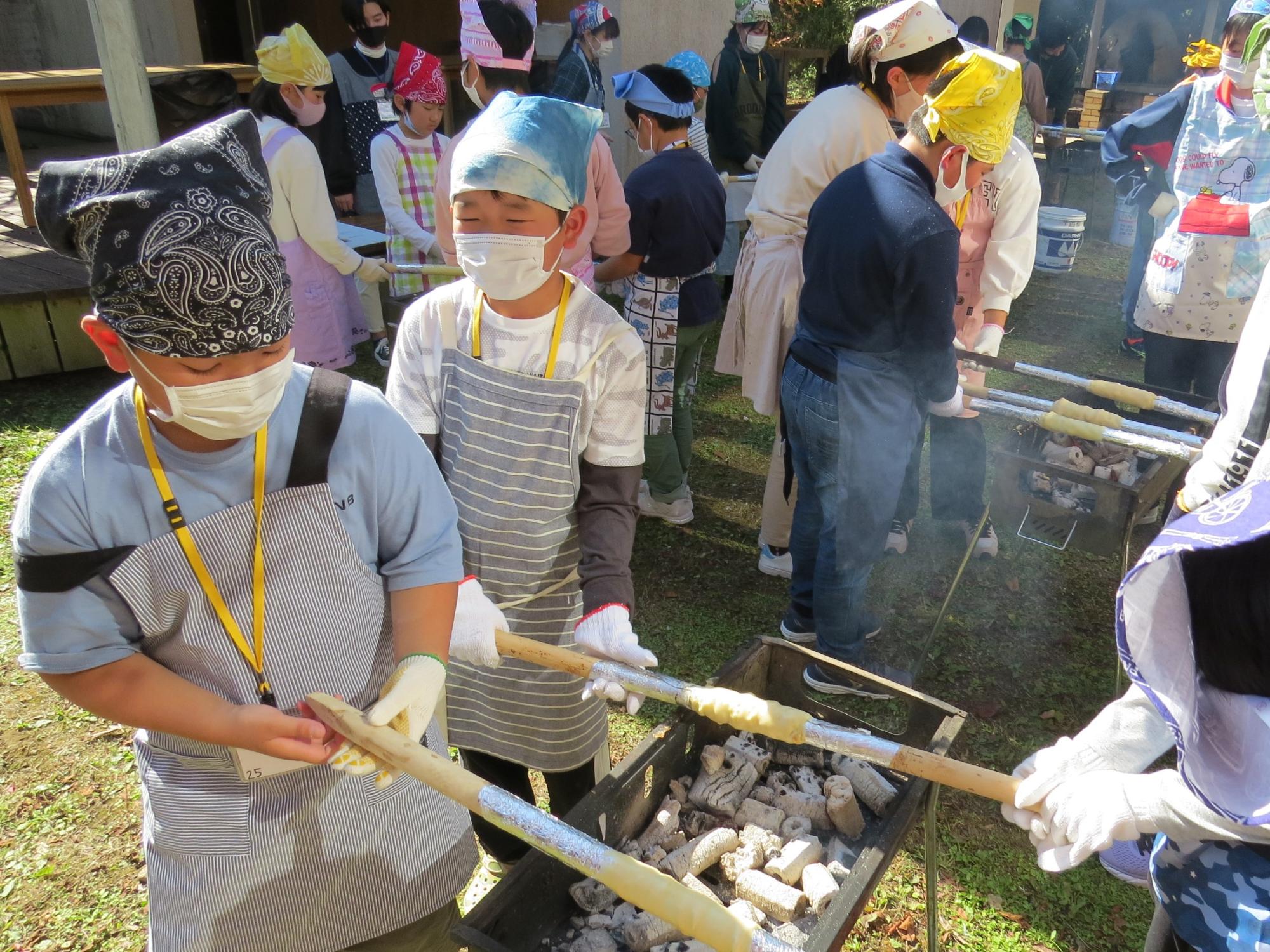 長い棒にアルミホイルをまきコンロで焼いている子どもたちの写真