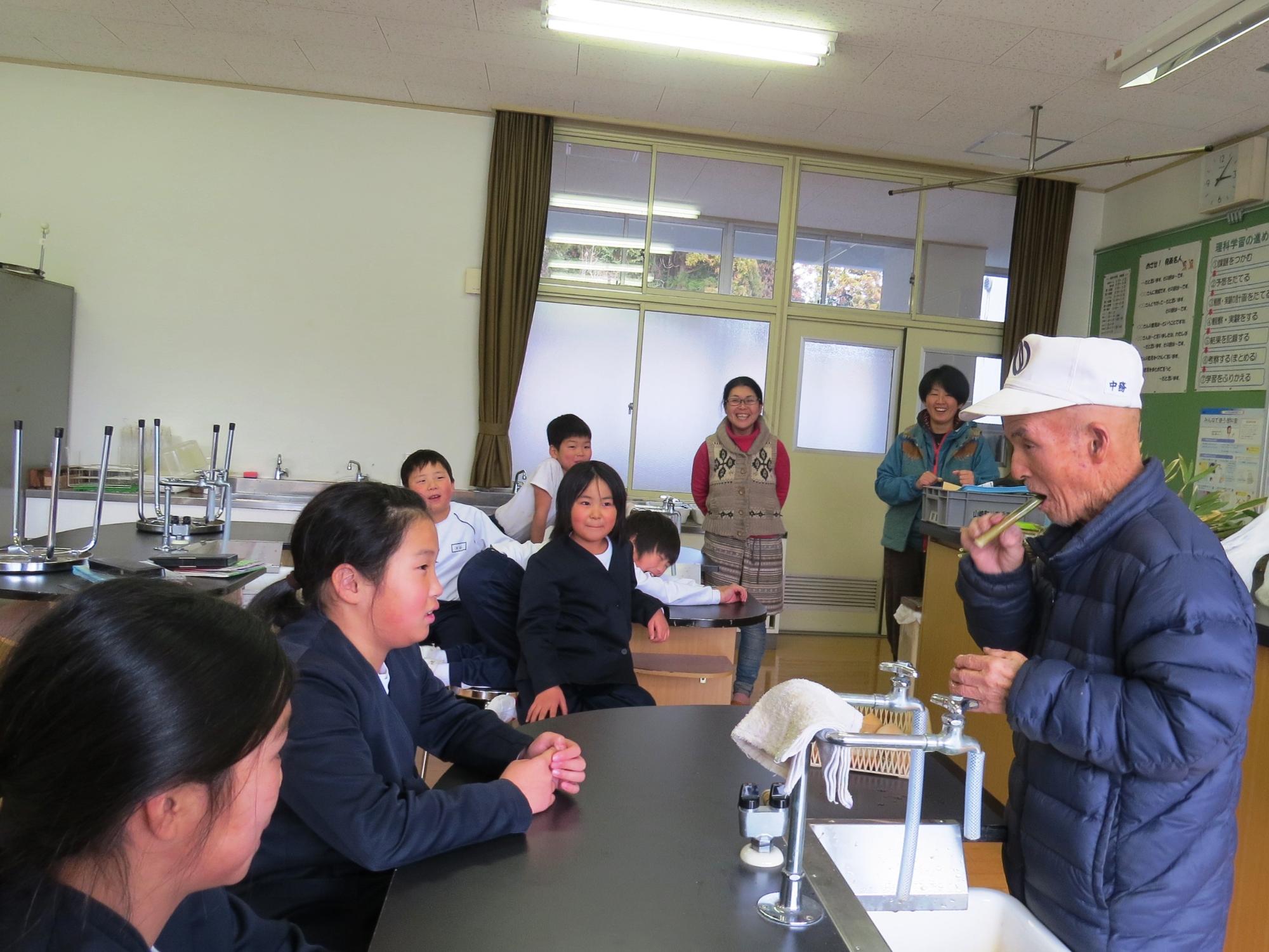 仲間あそび教室で、子ども達がボランティアさんから竹笛のつくり方を聞いている写真