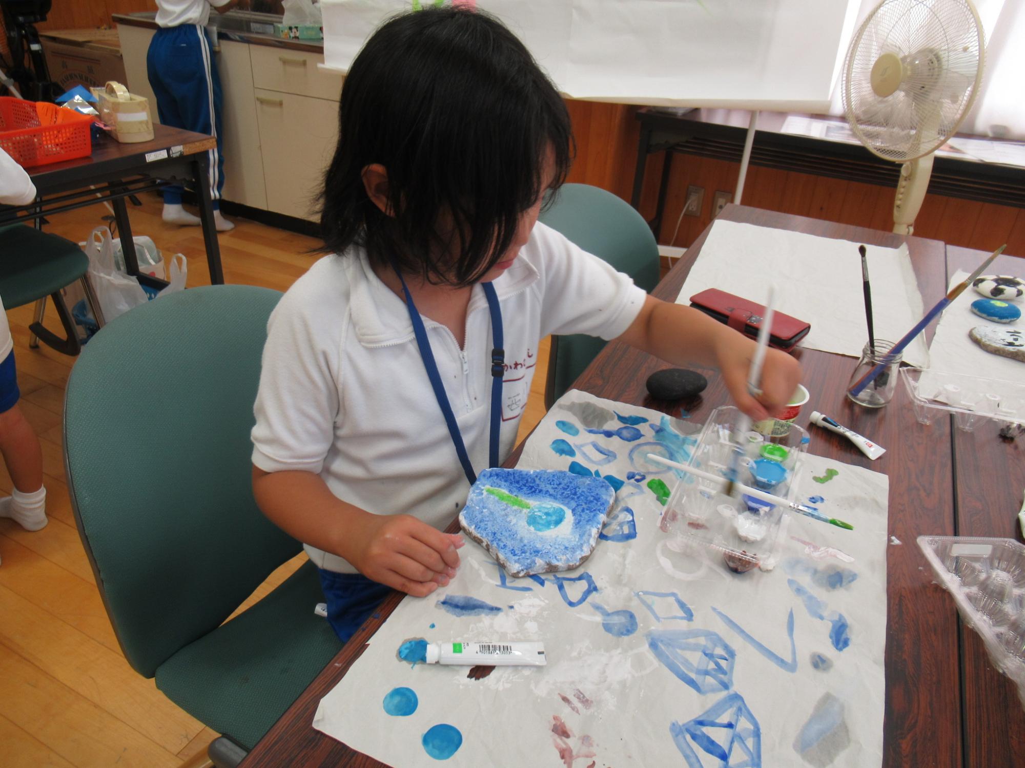 石ころアートに挑戦中の子どもが絵の具で石に色を付けている写真