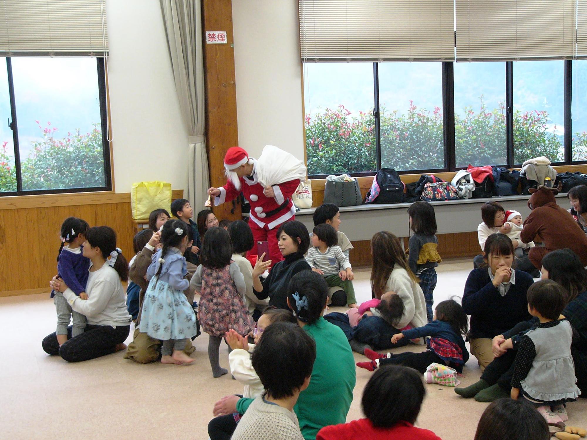 会場の子ども達にサンタクロースが鈴をならしてプレゼントを配っている写真