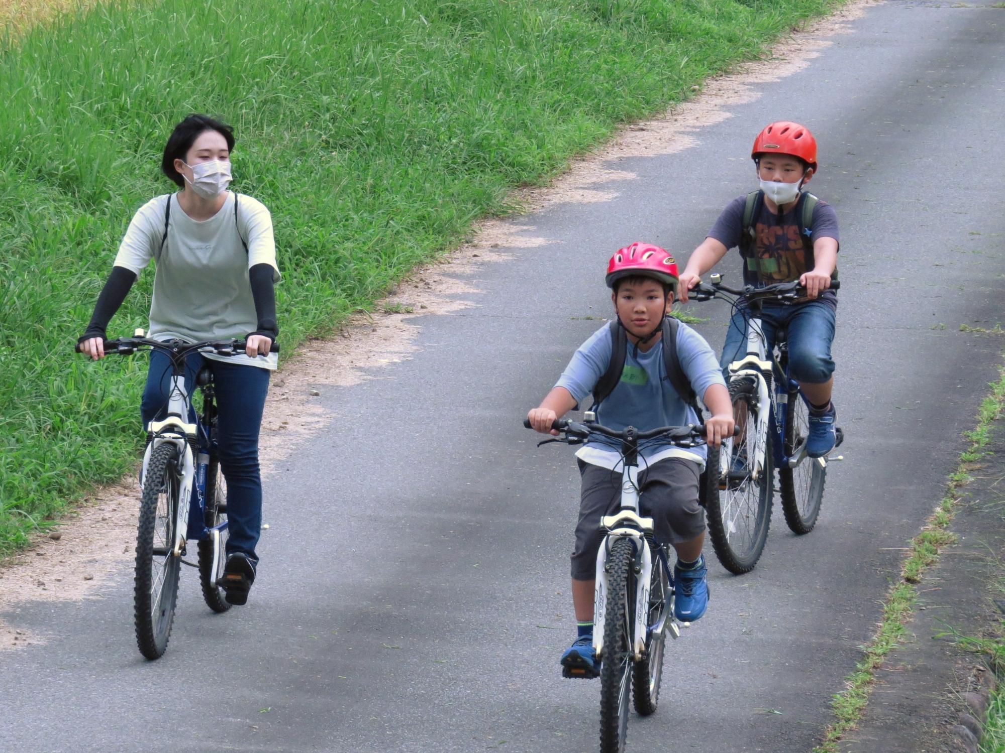 農道をさっそうと自転車で通過する子どもとサポーターの写真
