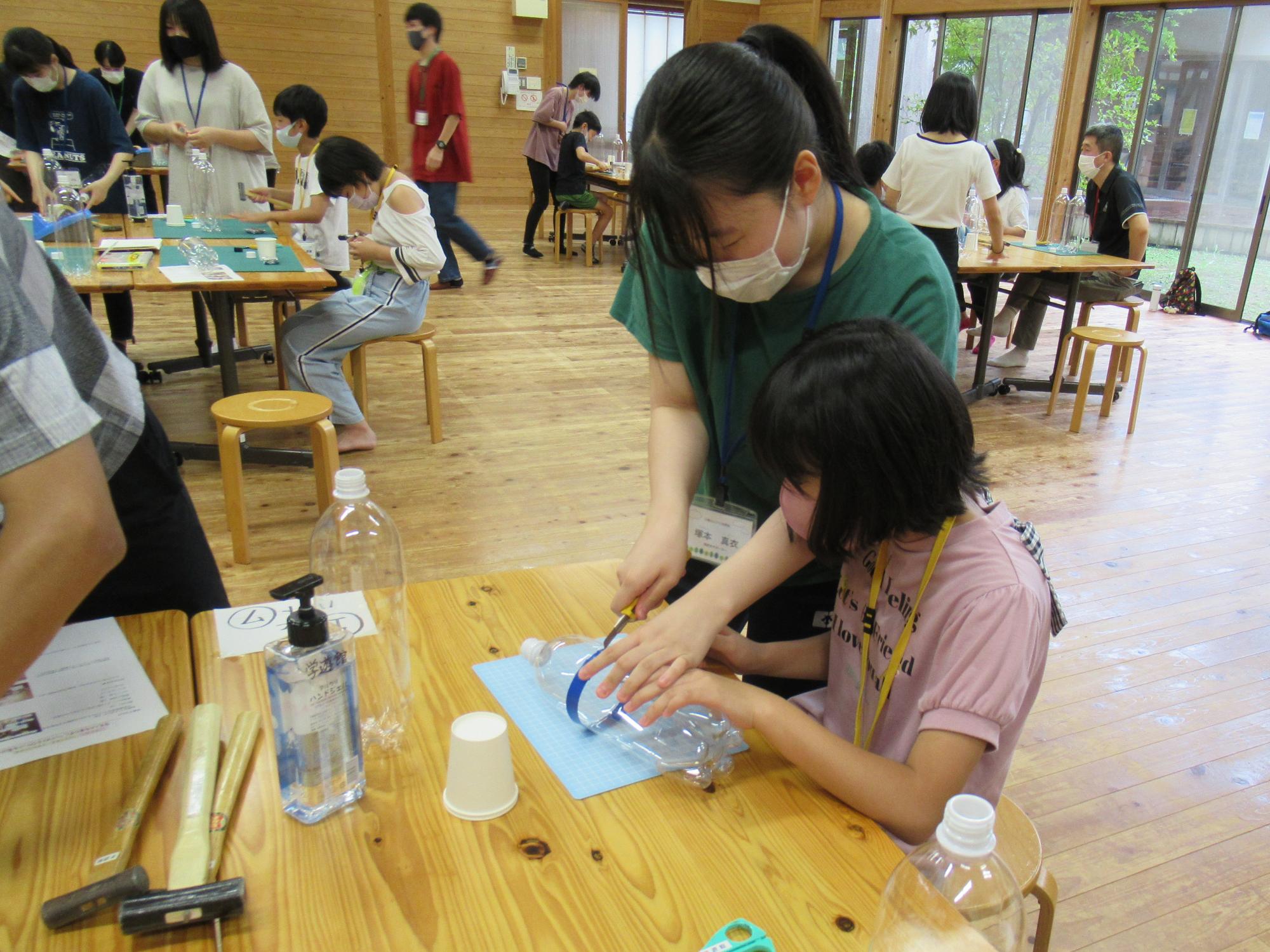 サポーターのお姉さんと一緒に、ペットボトルロケットづくりを頑張っている女の子の写真