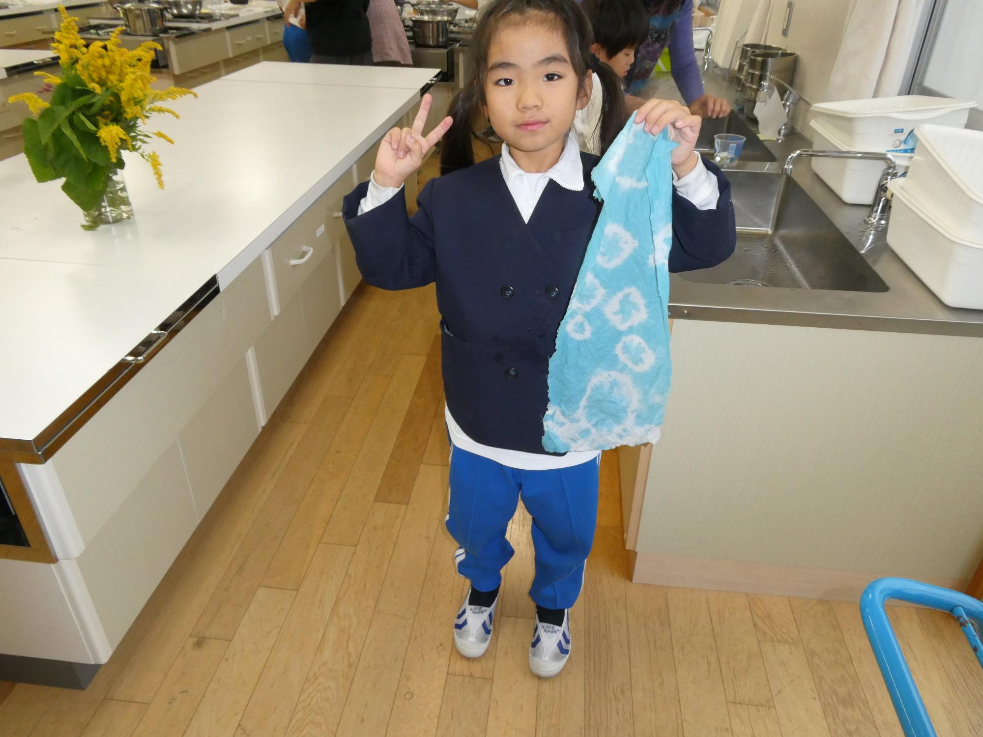 染め上がった布を広げてピースサインする子ども