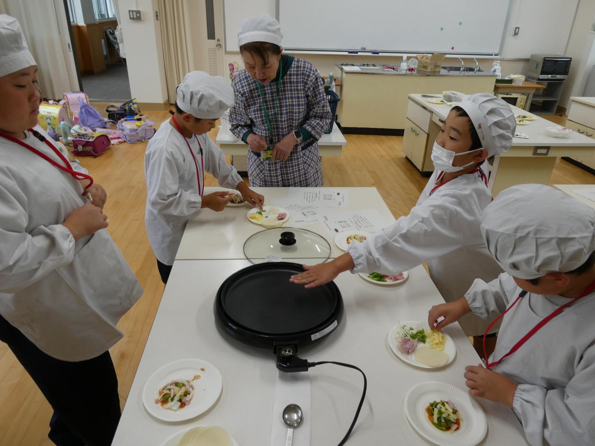 ホットプレートの温度確認と具をトッピングする子どもたち