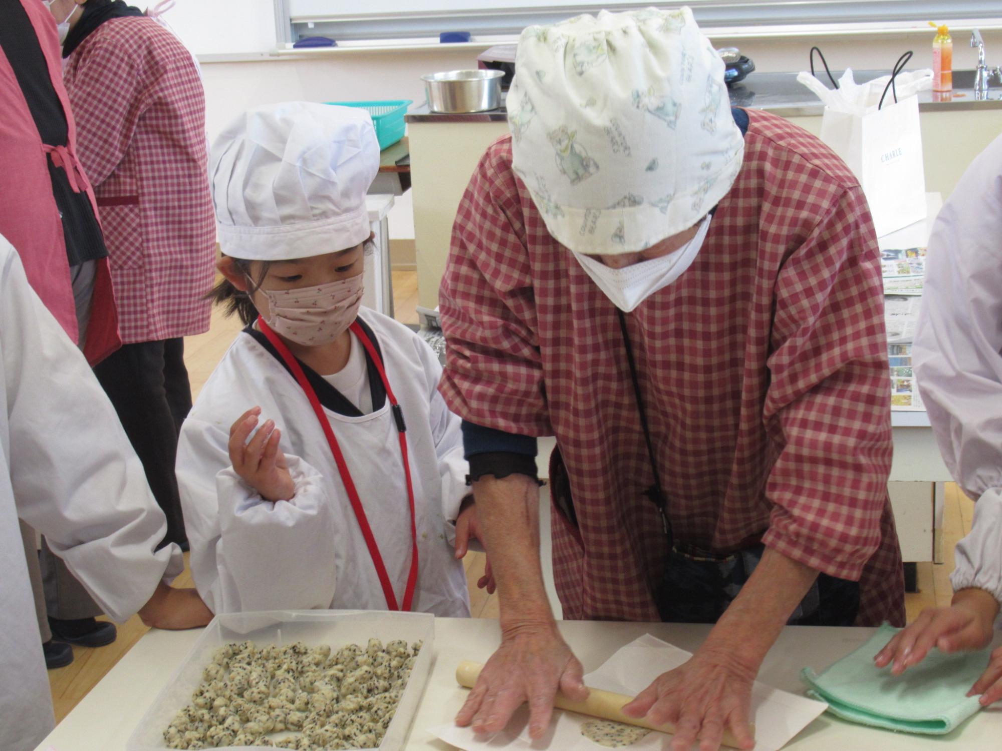 生地を麺棒で薄く伸ばす方法をサポーターが実演して小学生に見せている写真
