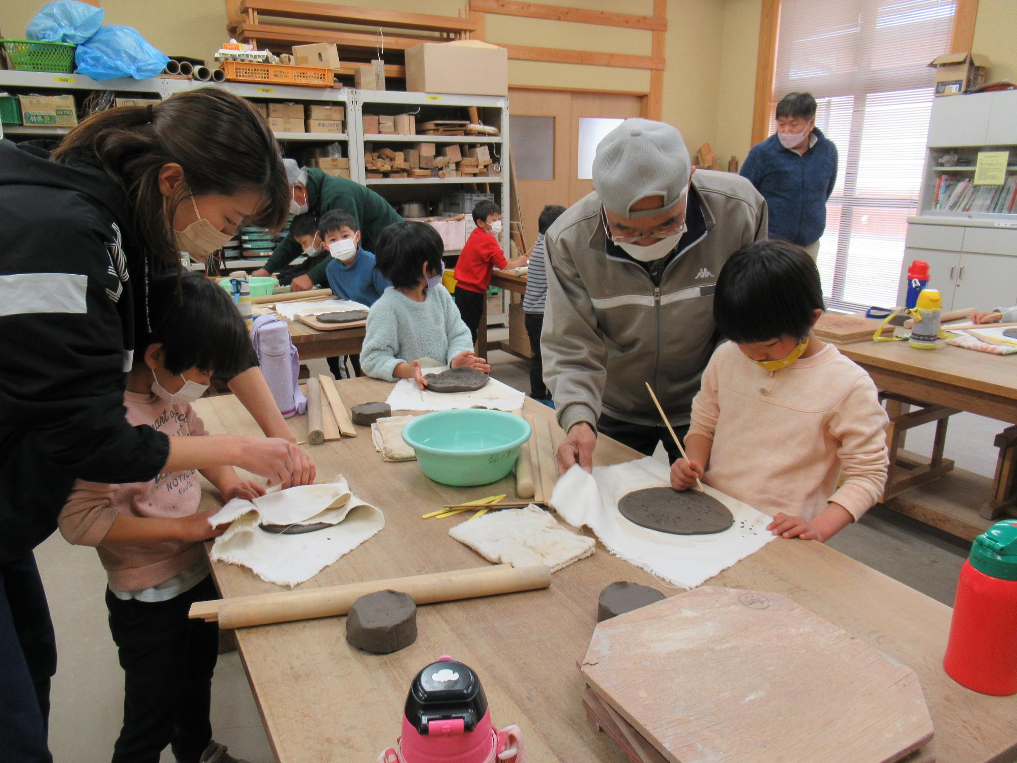 陶芸会の会員らが園児にお皿つくりを教えている写真