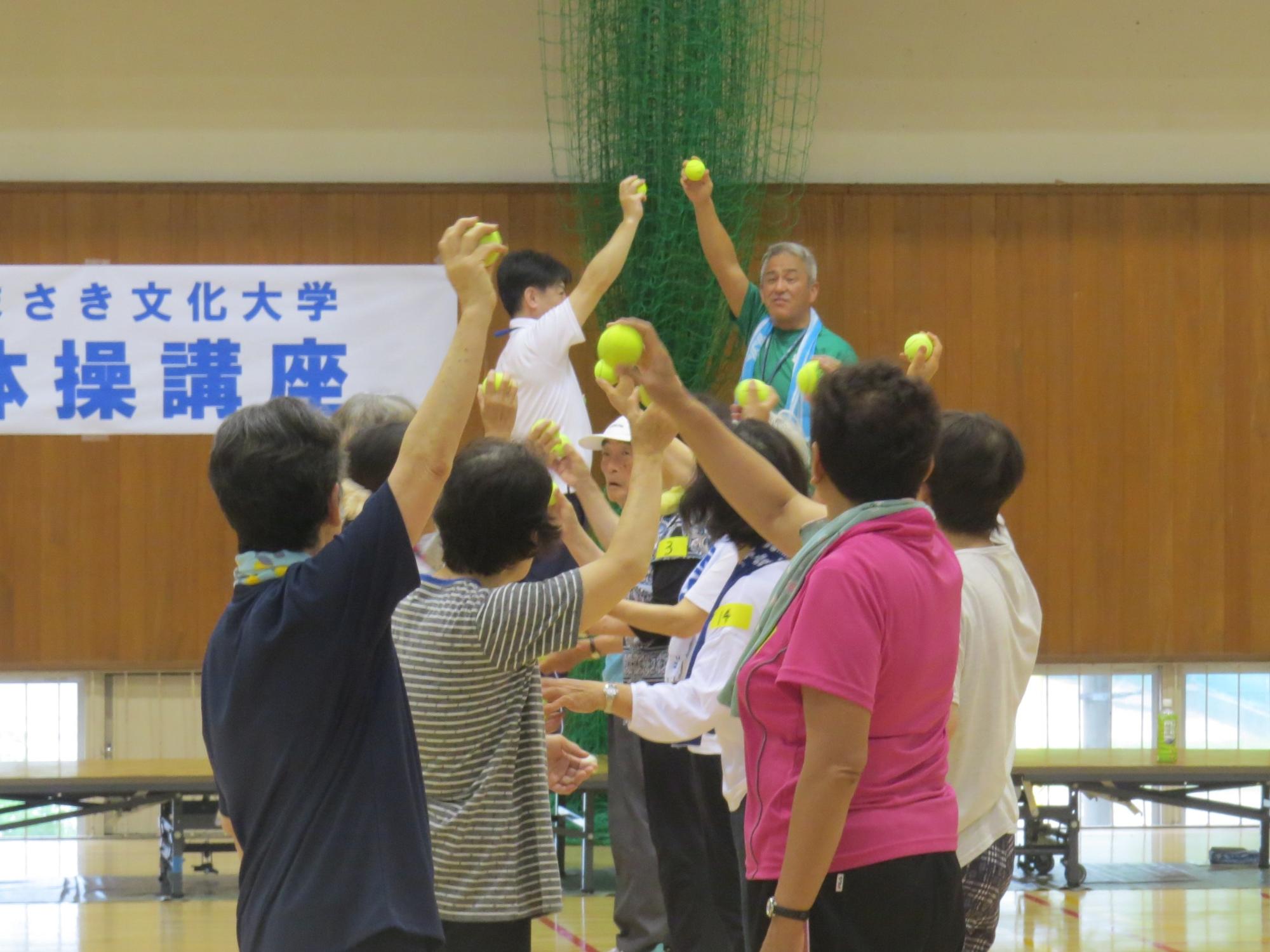 健康体操講座でテニスボールを持つ手を上げている写真