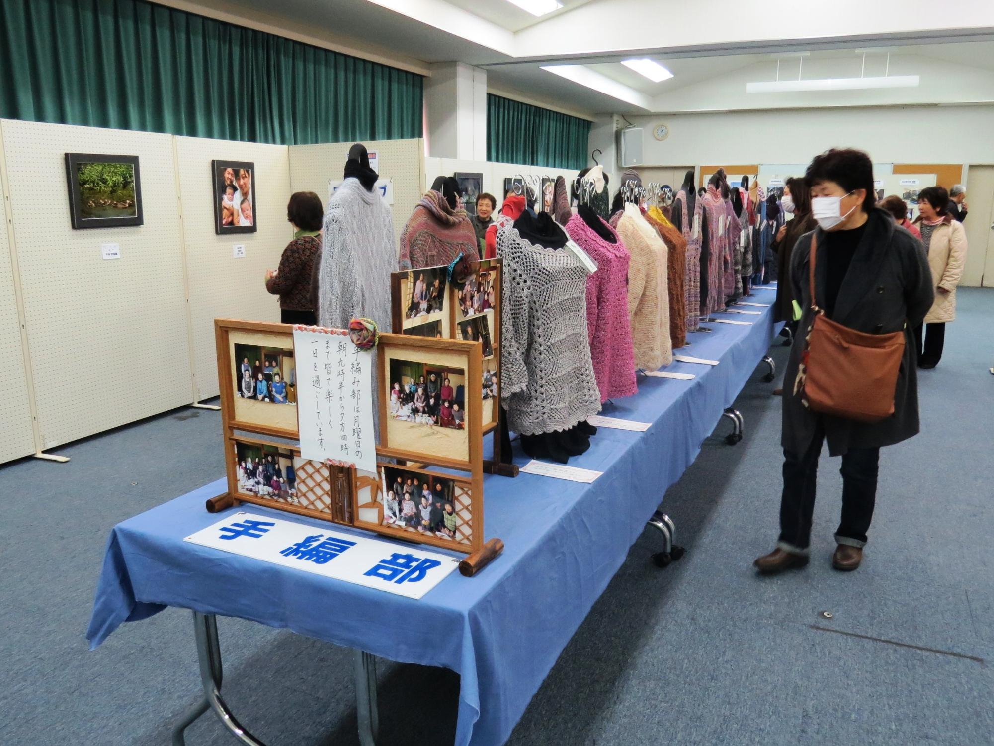 手編み部の展示で、たくさんの手編みの服が並んでいるのを見ている人の写真