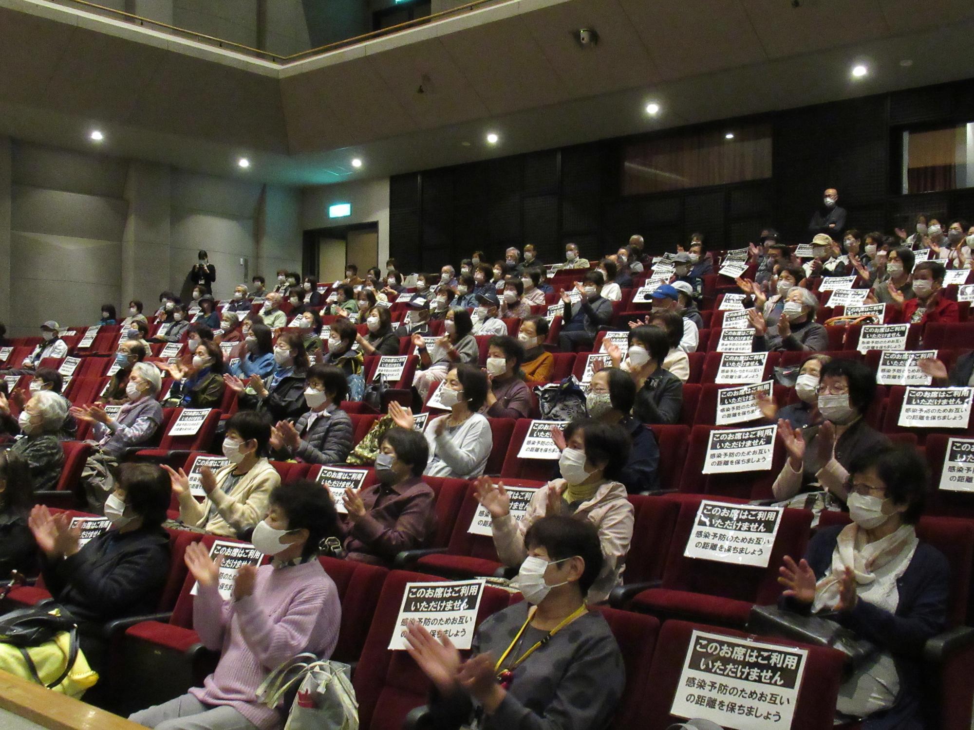 山崎文化大学の受講者らがホールの客席に座り和太鼓の音楽鑑賞を手拍子をとりながら楽しんでいる写真