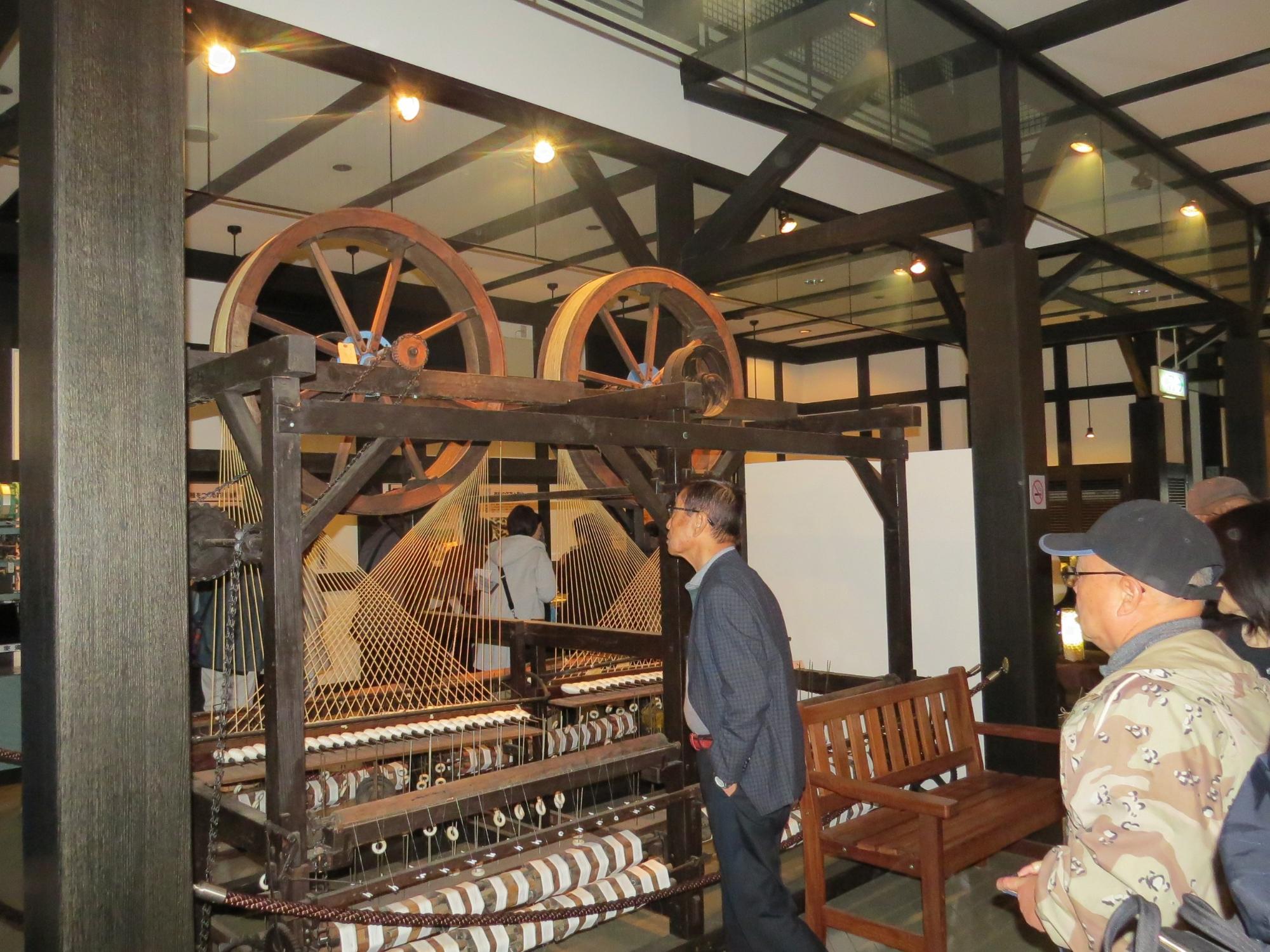 博物苑の建物内で蚕糸業で使用していた機械を熱心に見学する人の写真