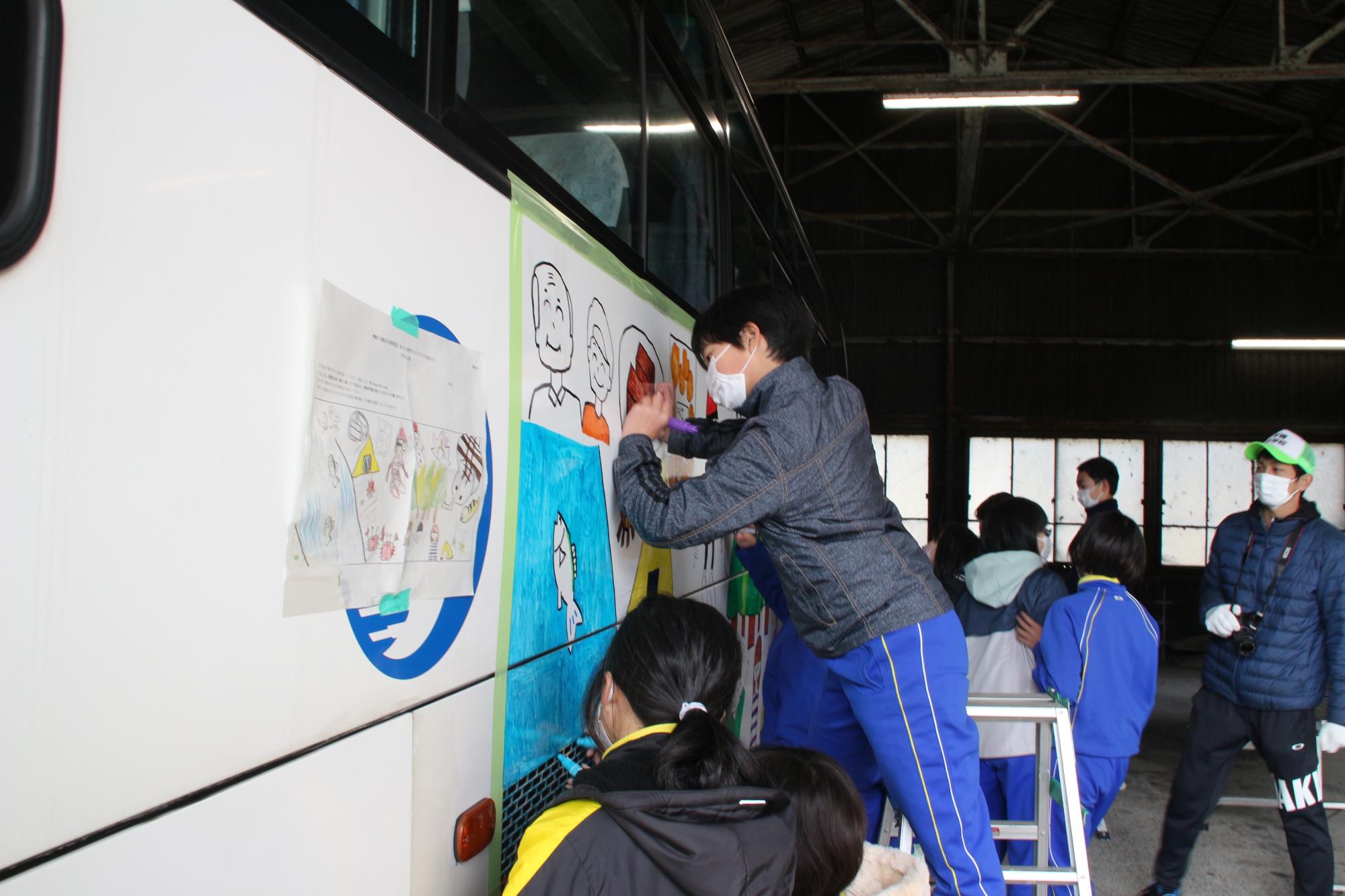 児童たちが高速バスの車体にマジックペンで絵を描き色を付けている写真