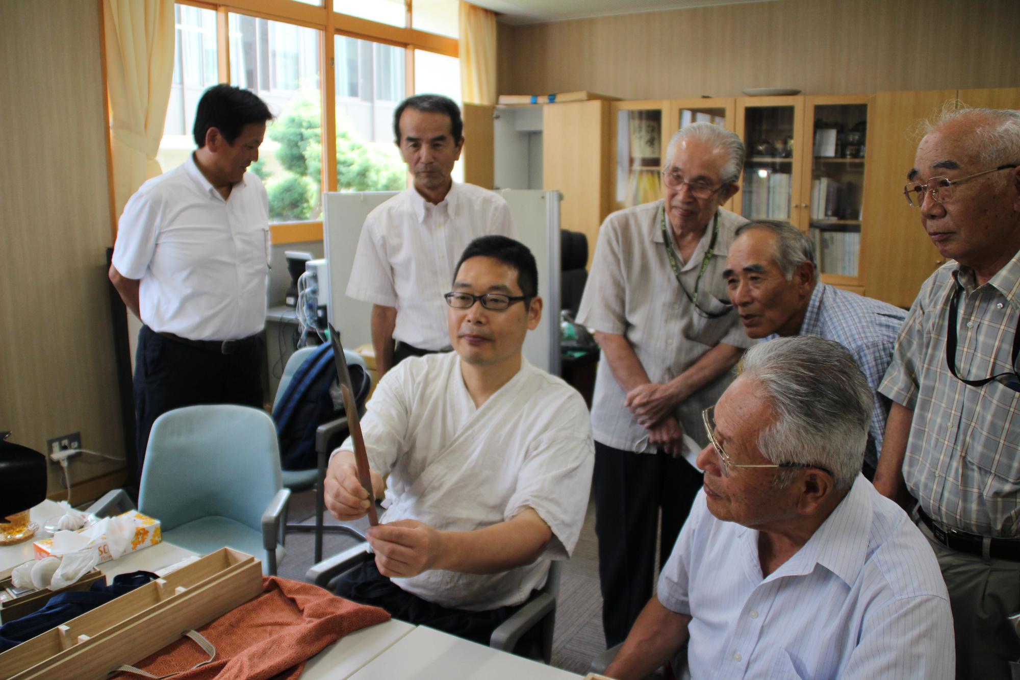 出来上がった短刀の説明をする刀鍛冶と話を聞く千草鉄の会のみなさんの写真