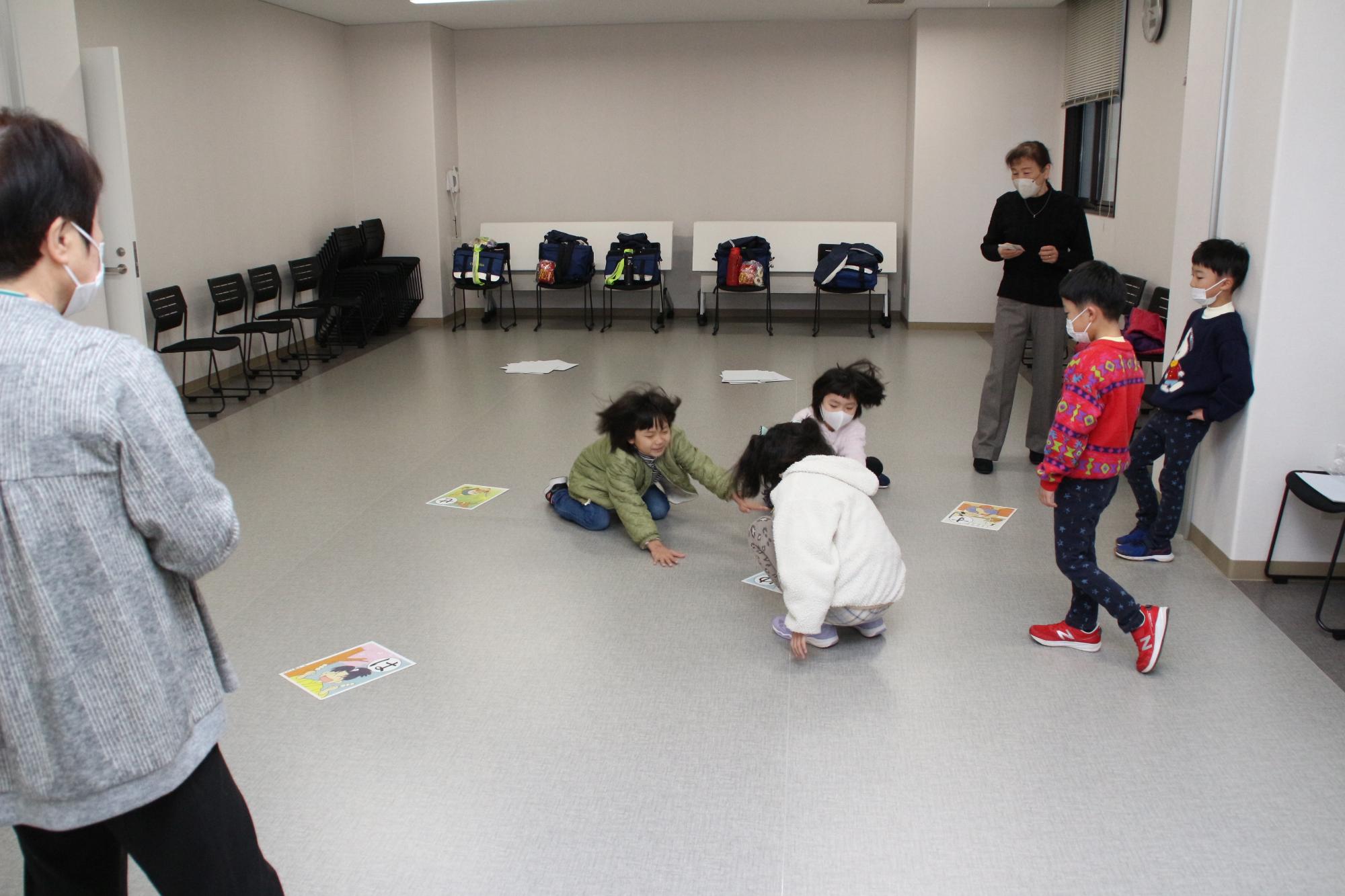 こども園の園児や小学校低学年の児童が手を伸ばして大きなサイズのかるたをとり合っている写真