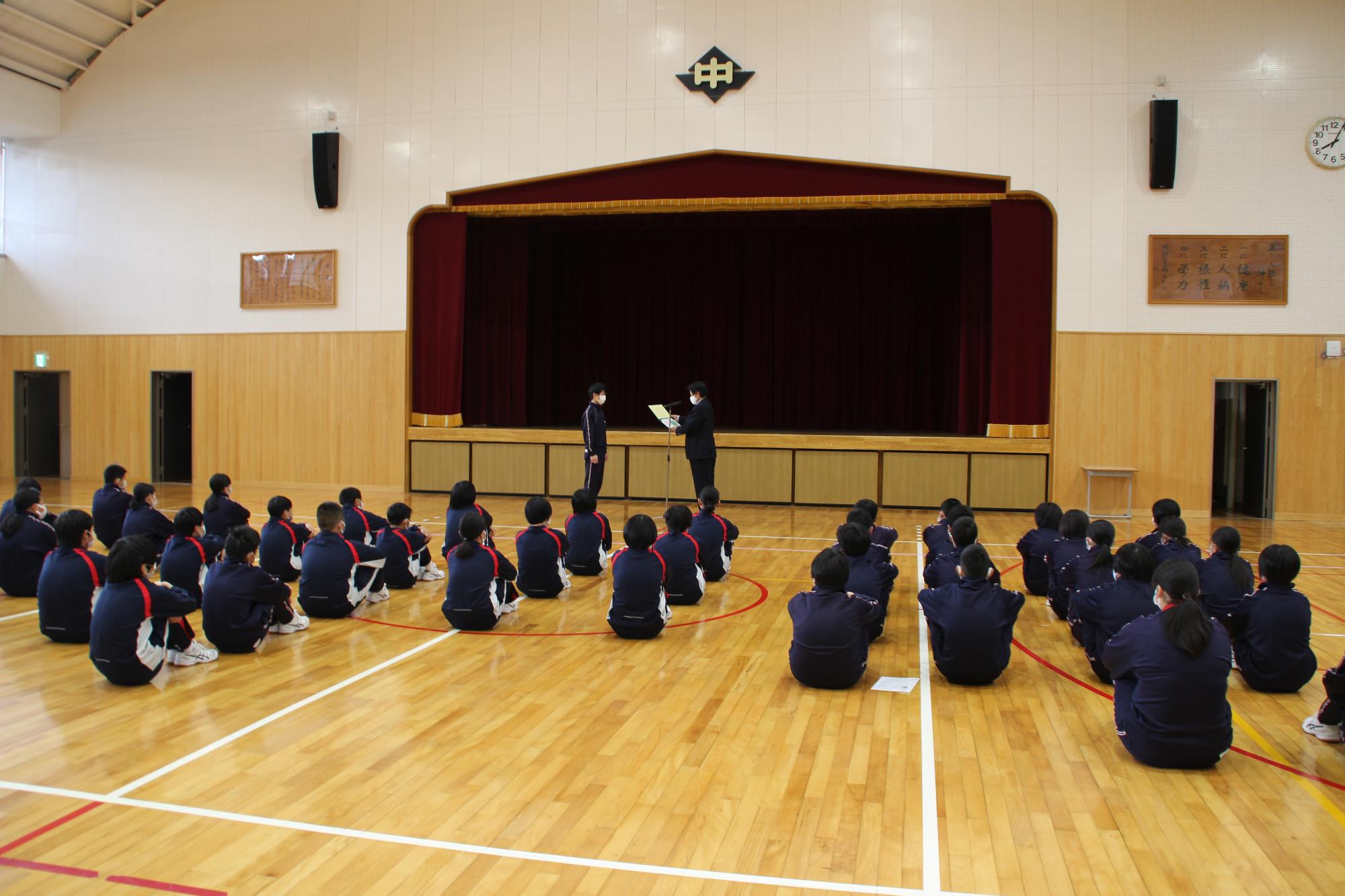 全校朝会で校長先生から生徒会長に賞状が授与される写真