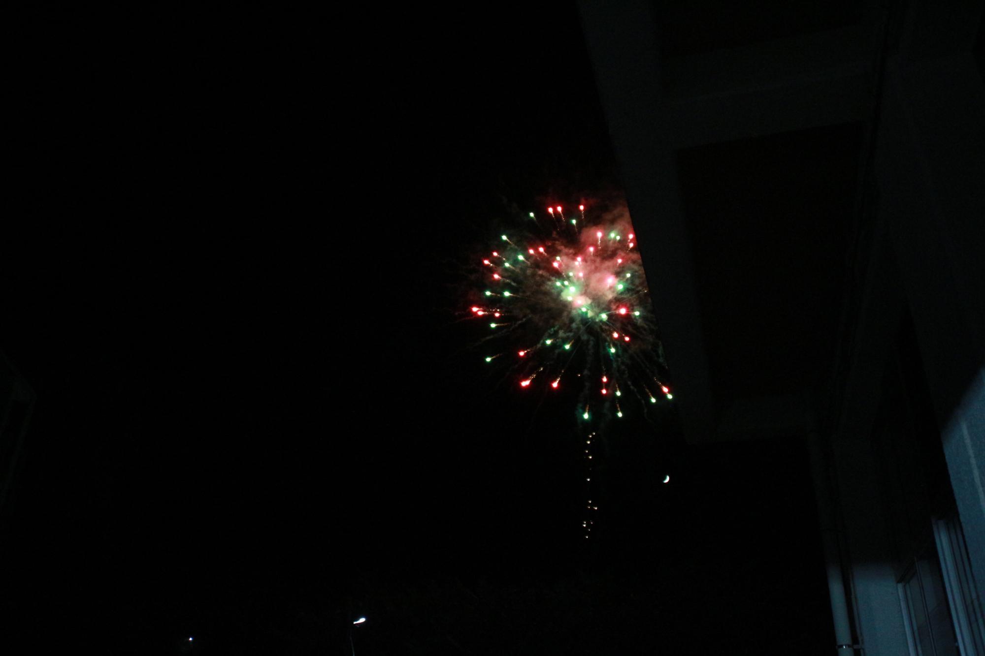花火が打ち上げられ、夜空に赤色や緑色の光の玉が広がっている写真
