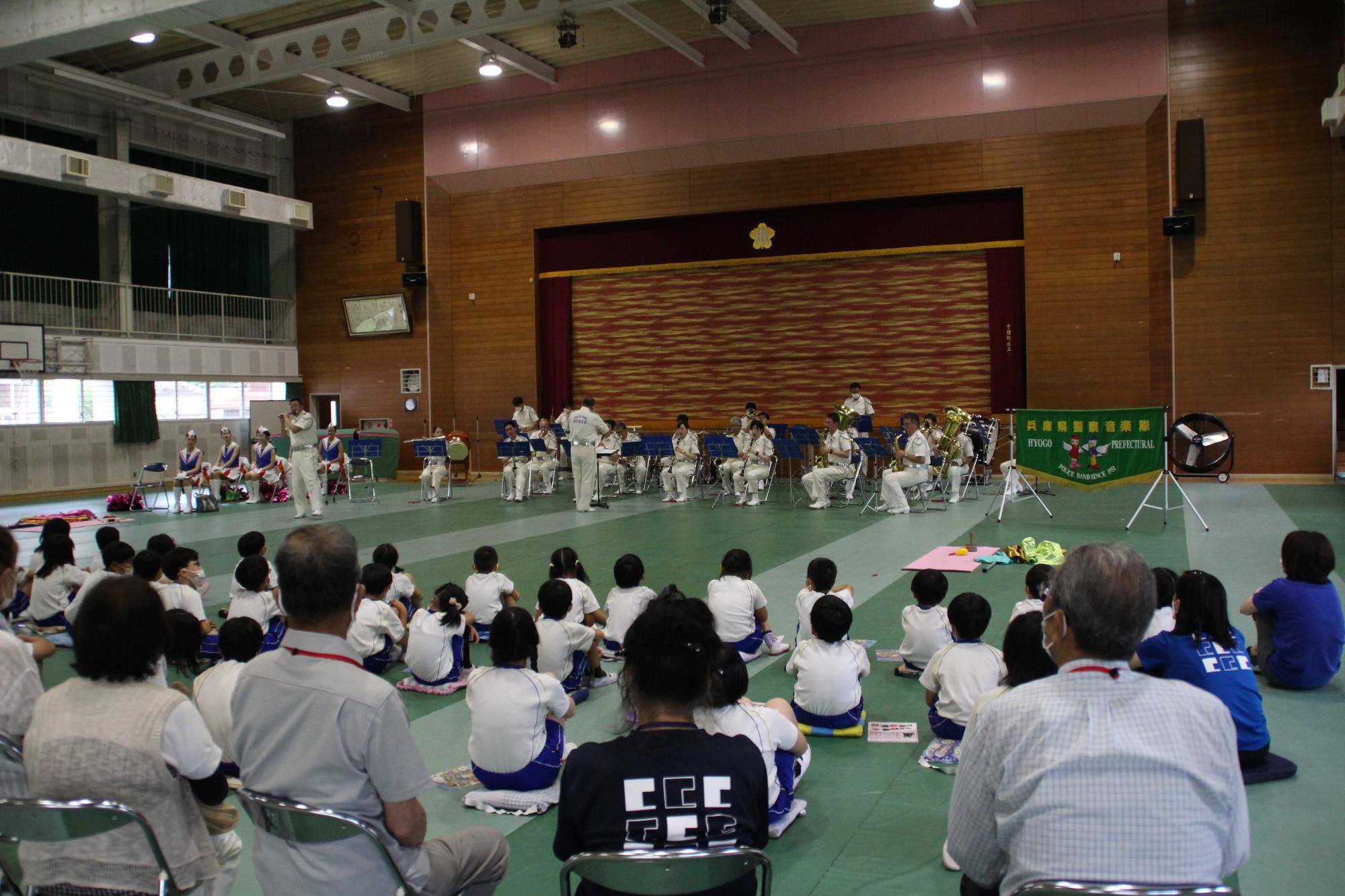小学校体育館でしきぐさ学園参加者と児童らの前で演奏を披露する兵庫県警音楽隊の様子