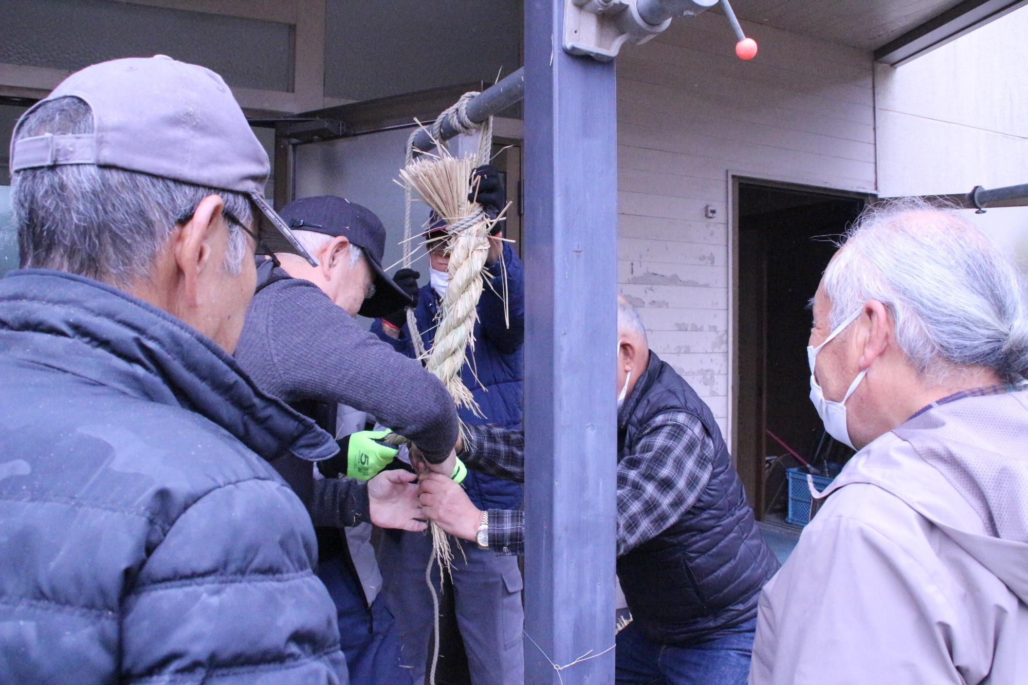 地元神社に奉納するための大きなしめ縄を老人クラブの会員4人がかりで作っている写真