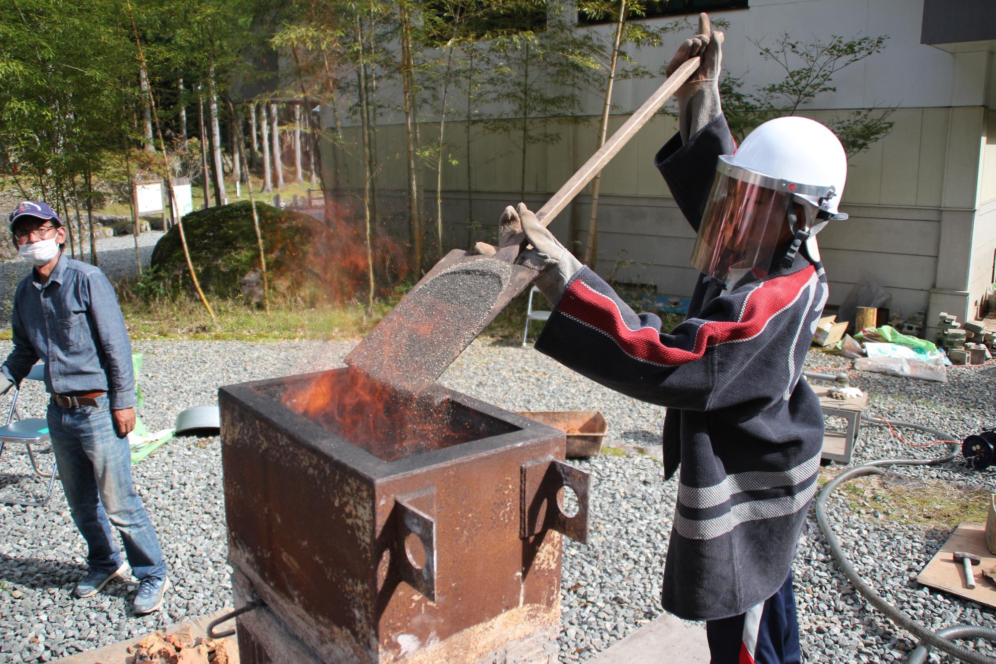 炭を燃焼している炉に砂鉄を投入する生徒の写真