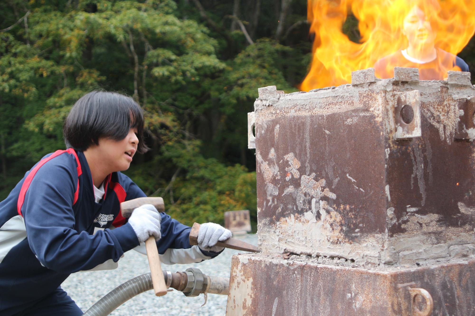 生徒が炭や砂鉄を投入して内部が燃えている炉の固定を解除している写真