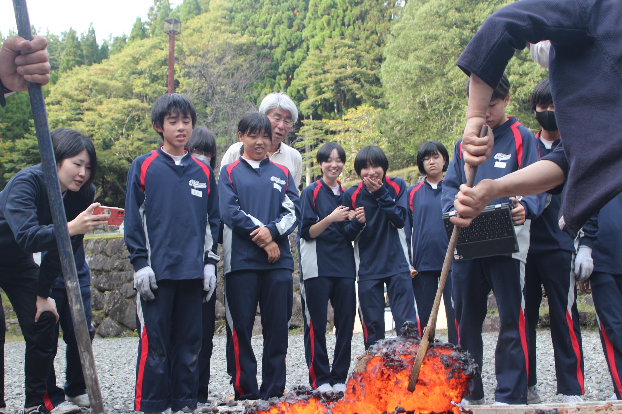 熱されたケラと呼ばれる塊を講師が取り出し、赤く溶け出すようなその塊を生徒らが興味深い様子で見ている写真