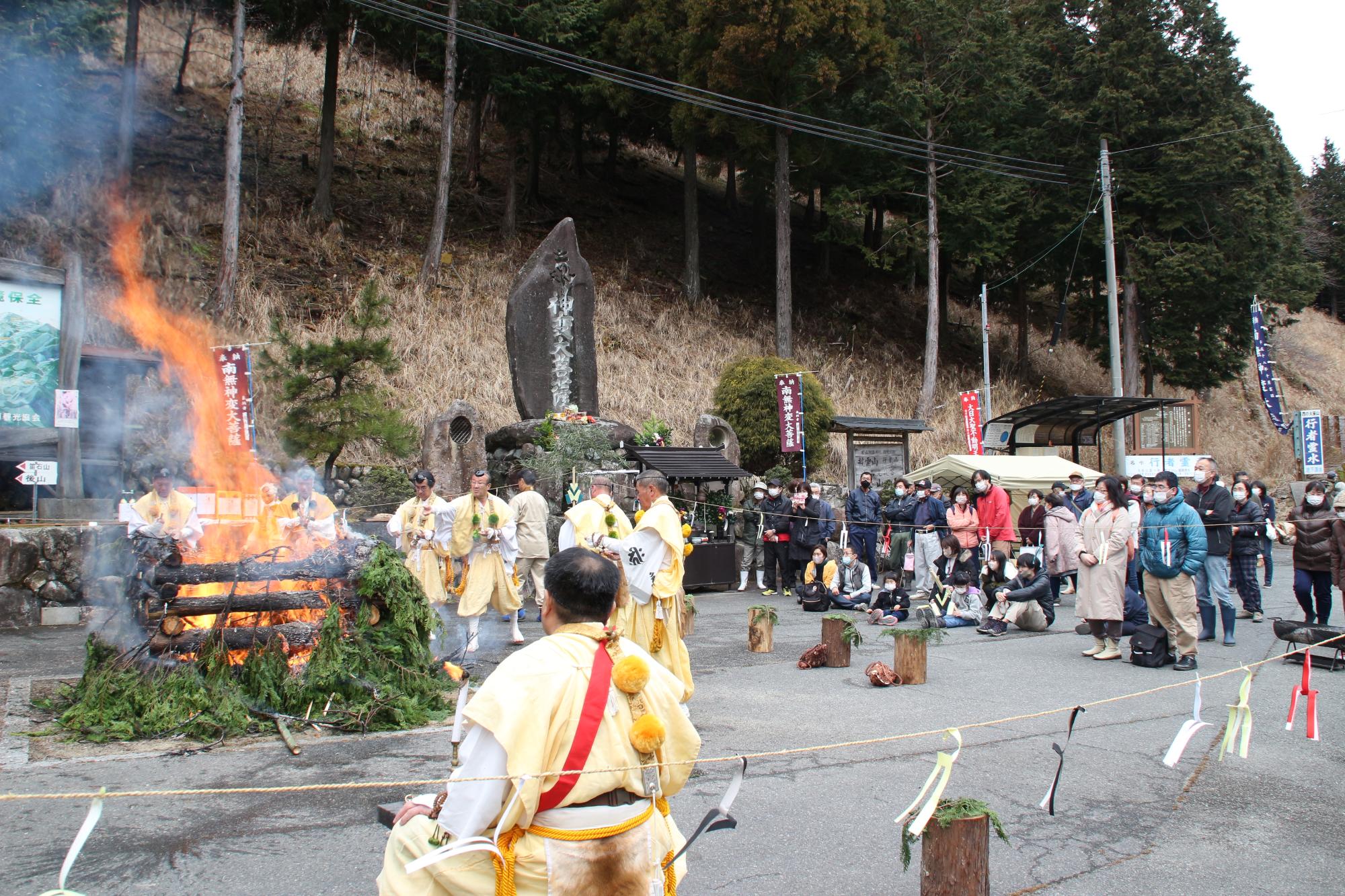 山伏が般若心経を唱えながらトンドの中へ護摩木を投げ入れている写真