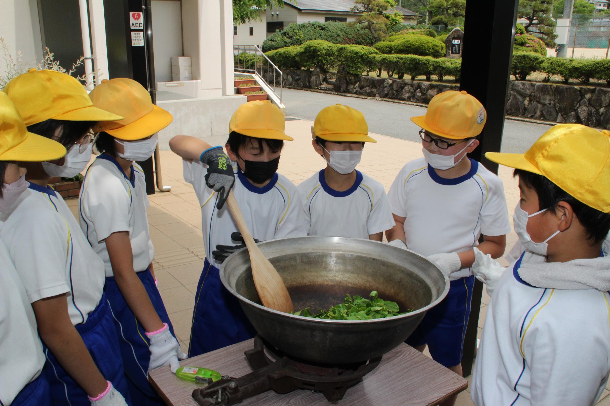 摘んだ茶葉を鍋で煎る作業をしている小学生の写真