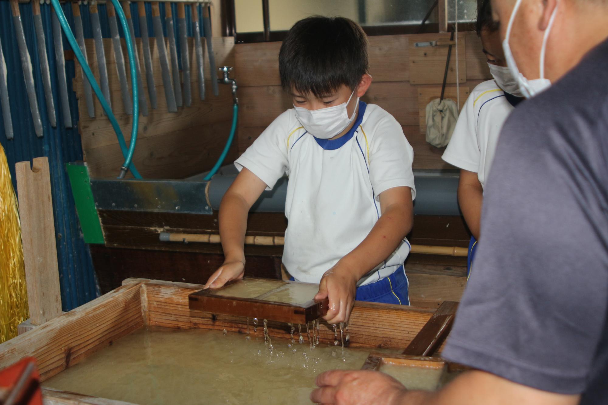 児童が水にさらした原料を専用の器具（すきけた）ですくっている写真