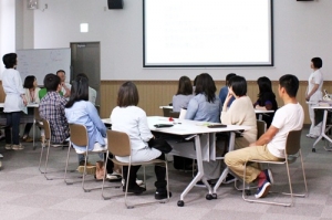 いくつかのグループに分かれて座り、前方のスクリーンを見ている参加者の写真