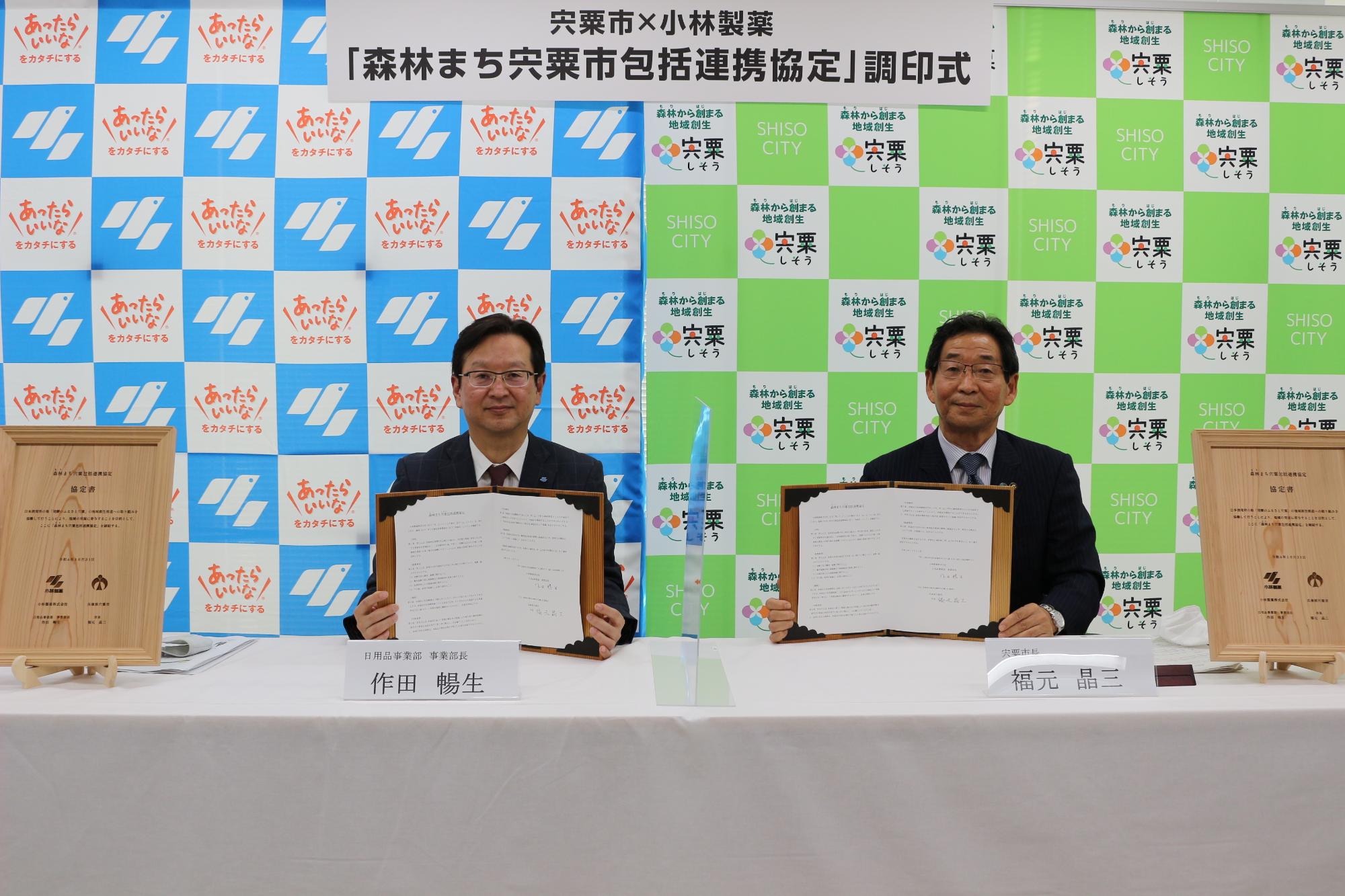 協定書を手に小林製薬の作田部長（左）と福元市長（右）が並んでいる写真