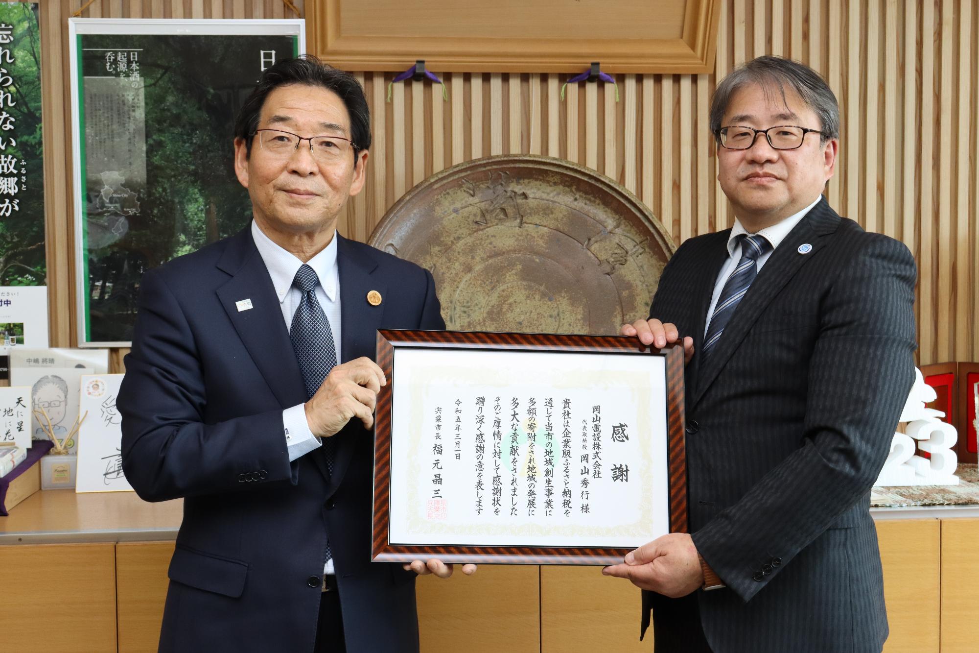 感謝状を手にした岡山電設株式会社代表取締役の岡山秀行様と福元市長の写真