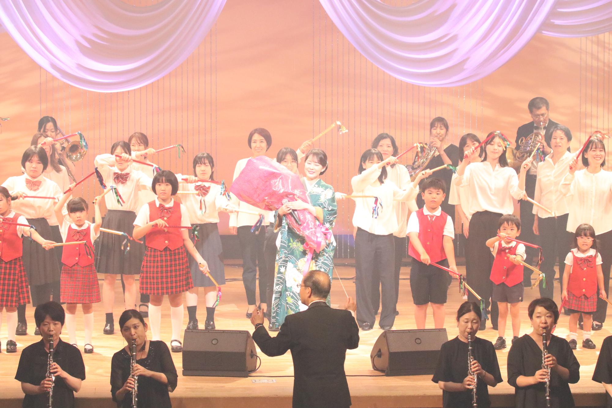 ステージ上で花束を持つ丘みどりさん、宍粟市少年少女合唱団ファミリーと宍粟市吹奏楽団