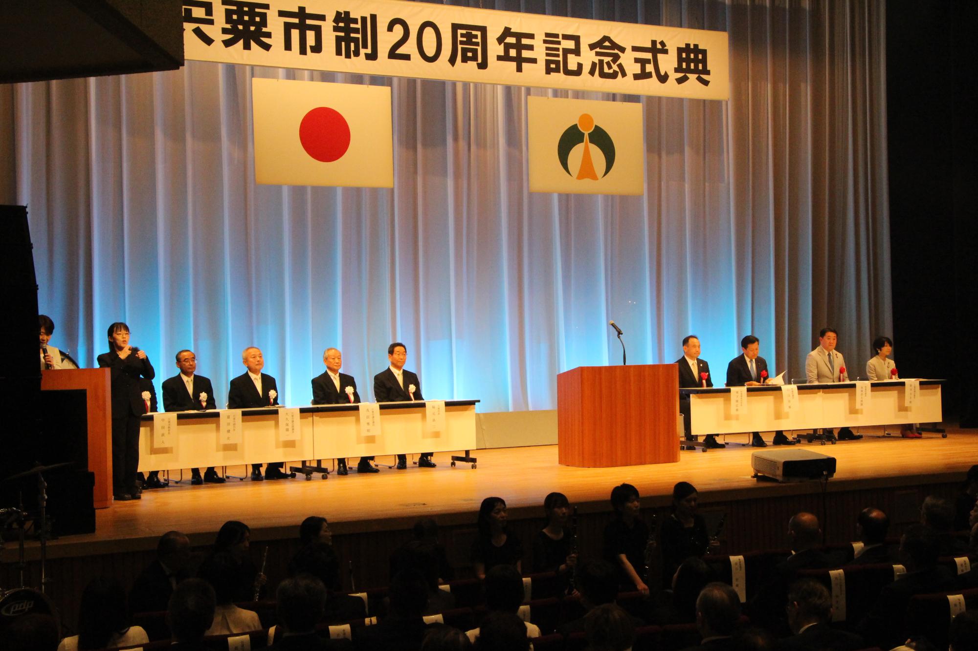 記念式典開式でステージに並ぶ市長、議長ら