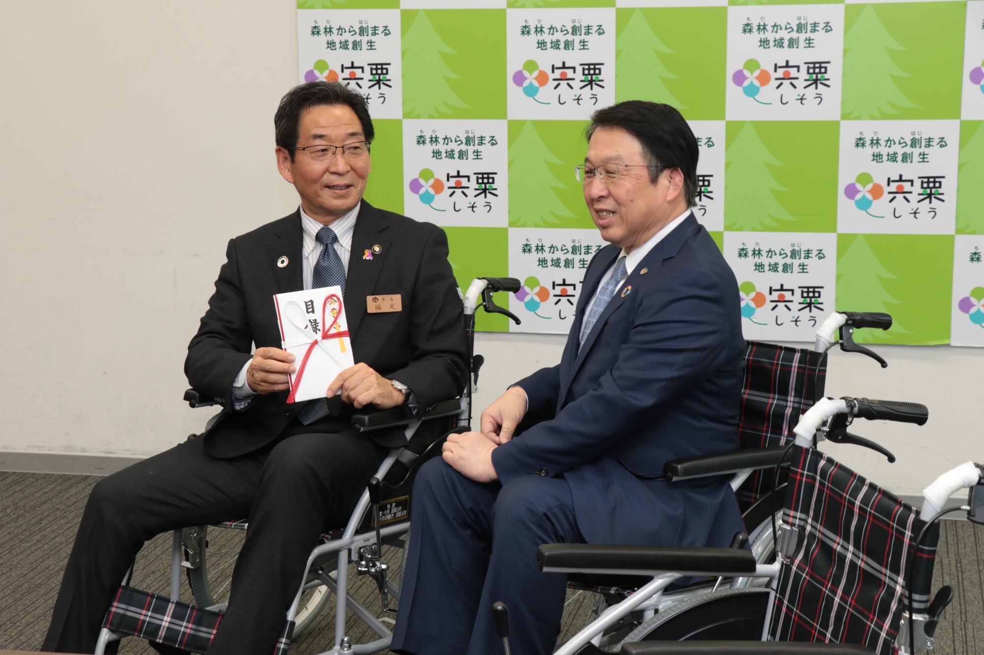 左は目録を手にした福元市長、右は株式会社第一生命姫路支社長が寄贈された車いすに座っている写真