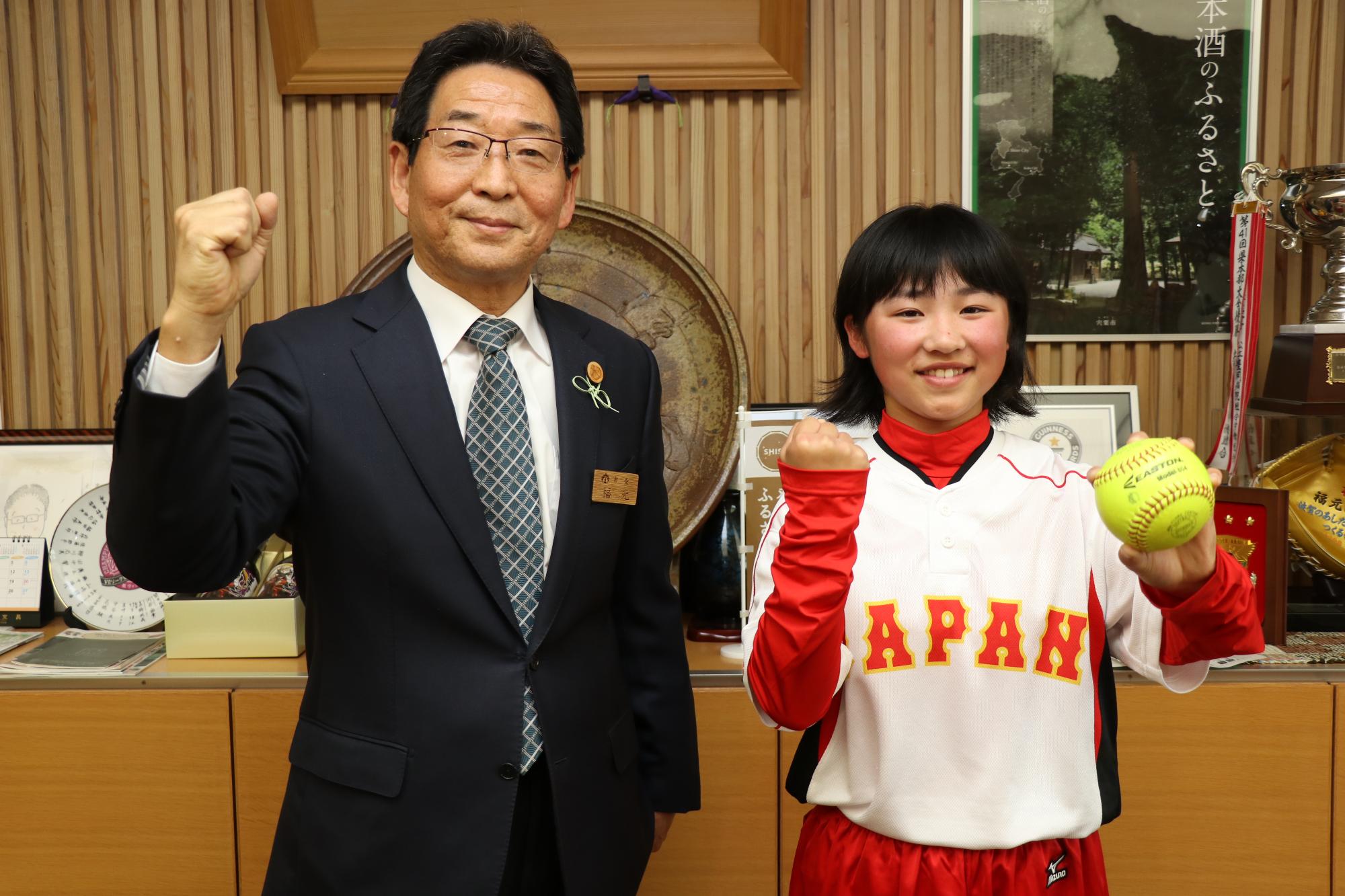 ソフトボールを手にした實友選手と福元市長がガッツポーズで並んでいる写真