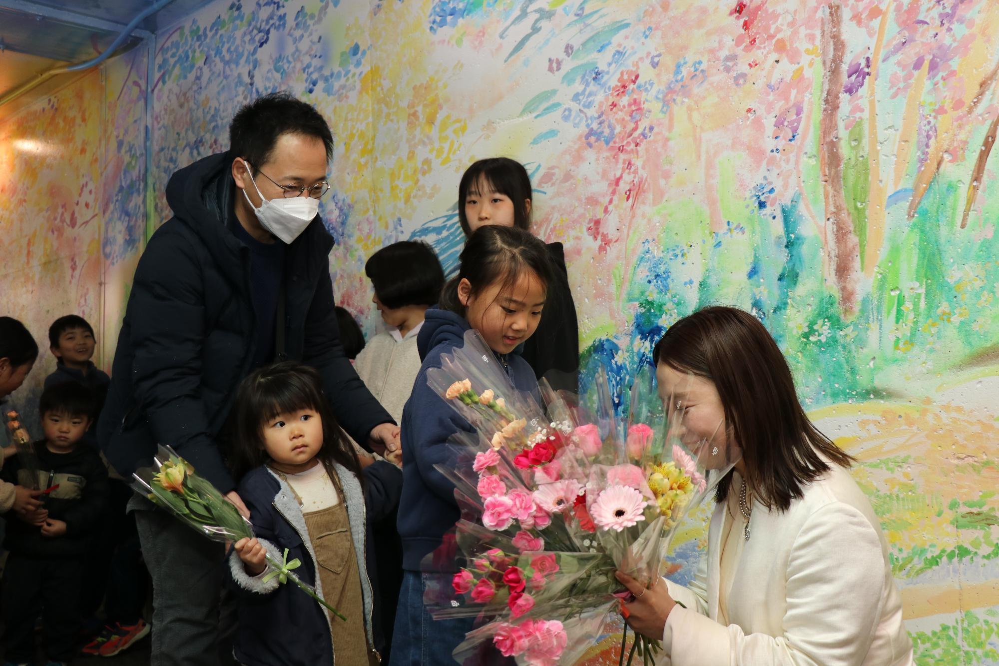 シソラミチを制作した植田志保さんが子どもたちから花を受け取っている写真